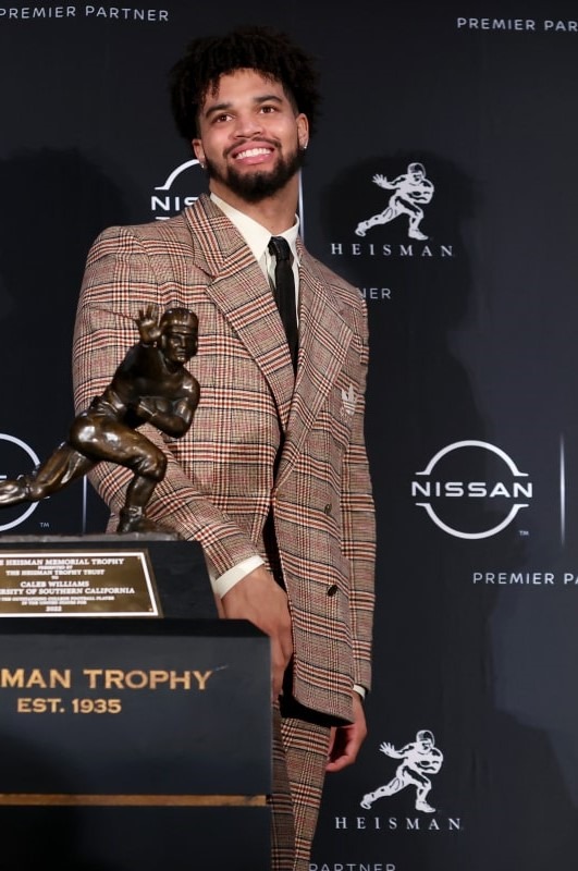 Caleb Williams standing next to the Heisman Trophy at an award ceremony.